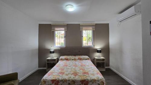 a bedroom with a bed with two night stands and two windows at Tajy Iguazu Hotel in Puerto Iguazú