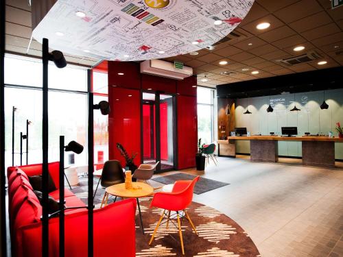 a lobby with red chairs and a table and a counter at Ibis Poznan Polnoc in Suchy Las