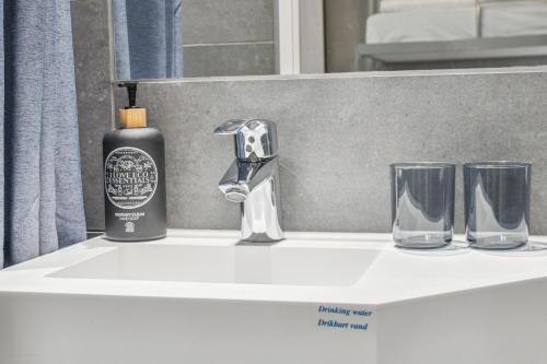 Un lavabo de baño con una botella de jabón y dos vasos. en Hotel Fyrtøjet, en Odense