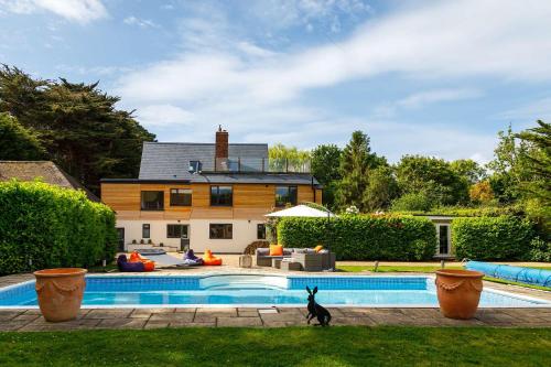 a dog walking by a pool in front of a house at Stunning 5BR Home with Pool - 5 min to Beach in West Wittering