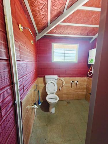 a bathroom with a toilet and red walls at Lalitha Farm Stay in Tumkūr