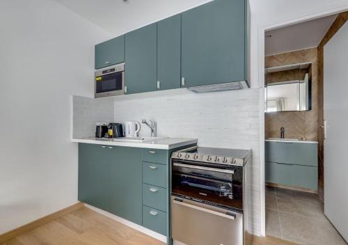 Elle comprend une petite cuisine avec des placards bleus et un évier. dans l'établissement Sur un nuage - Calme & Rénové - Odéon, à Paris