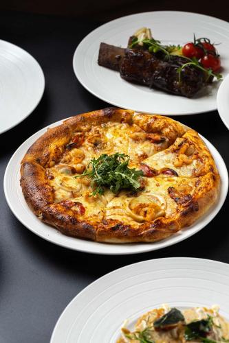 a pizza on a plate with other plates of food at Levatio Suites Muscat, a member of Radisson Individuals in Muscat