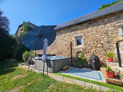 a hot tub with an umbrella next to a building at Gîte de La Garrigue in Brandonnet