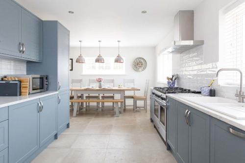 a kitchen with blue cabinets and a dining table at Beach house for 10 with hot tub & garden in West Wittering