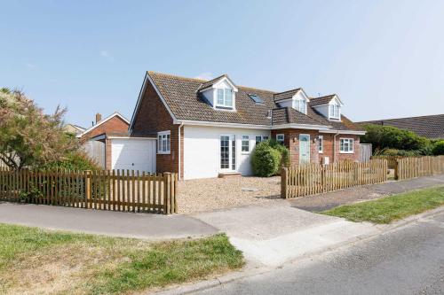 a brown and white house with a wooden fence at Beach house for 10 with hot tub & garden in West Wittering