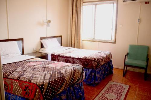 a room with two beds and a chair and a window at Hotel Aljazira in Nouadhibou