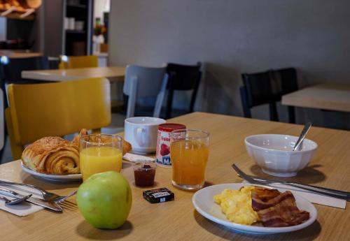 a table with a plate of breakfast food and orange juice at B&B HOTEL AVRANCHES Baie du Mont St-Michel in Le Val-Saint-Père