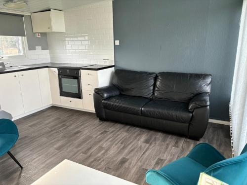 a living room with a black leather couch in a kitchen at Chalet 75 in Mundesley