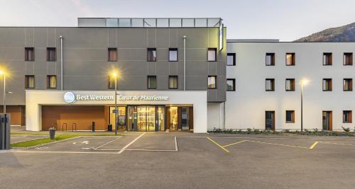 a building with a parking lot in front of it at Best Western Coeur de Maurienne Hotel Restaurant & Spa in Saint-Jean-de-Maurienne