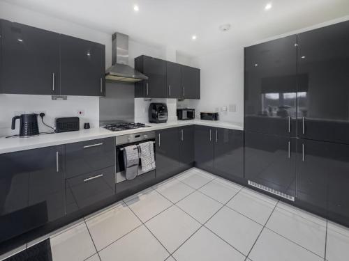 a kitchen with black cabinets and white tile floors at Sleeps 8 with Garden and Pet Friendly in Ashford