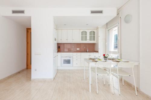 a kitchen with white cabinets and a table and chairs at Nova Apartment by Hello Homes Sitges in Sitges