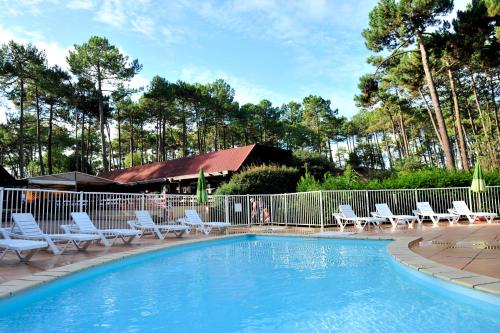 una piscina con sillas blancas y una valla en VTF Les Bruyères, en Maubuisson