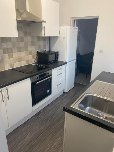 a kitchen with white cabinets and a sink and a refrigerator at Happy Homes in Stoke on Trent