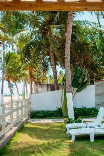 a group of white lounge chairs under palm trees at Pousada Fenícia in Japaratinga