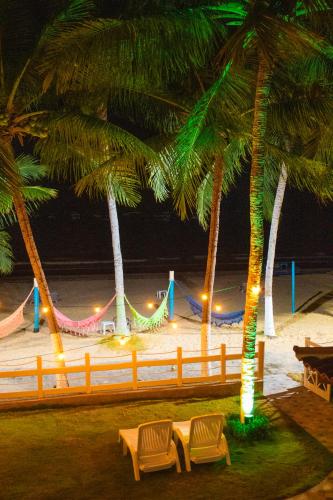 two chairs under palm trees on a beach at night at Pousada Fenícia in Japaratinga