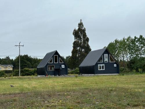two black houses in a field in a field at Cabañas RyL2 in Puerto Montt