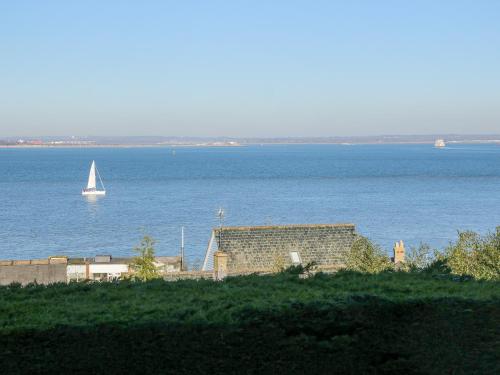 a sail boat in the water with a building and a boat at High Tide in Cowes