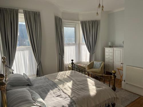 a bedroom with a bed and a chair and windows at Cliftonville House in Whitstable