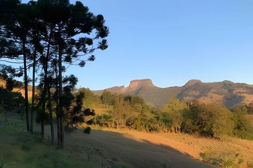 a dirt road with trees and mountains in the background at Chalés Suítes Gorjeios da Mantiqueira in São Bento do Sapucaí