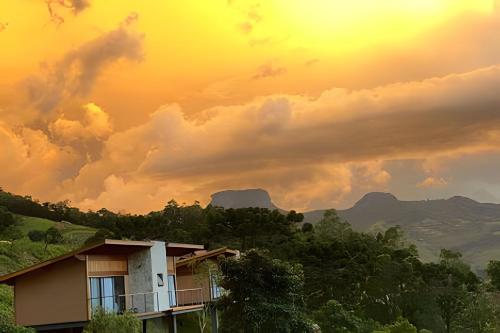 a house on a hill with the sunset in the background at Chalés Suítes Gorjeios da Mantiqueira in São Bento do Sapucaí
