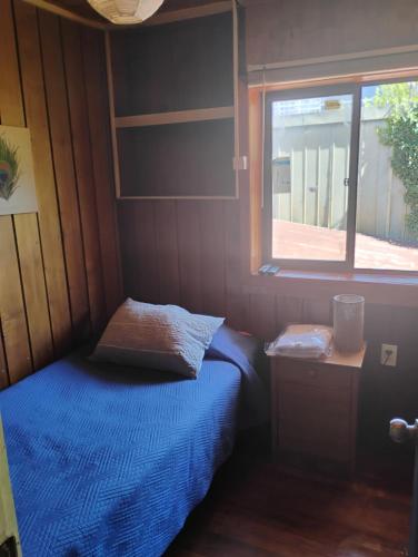 a small bedroom with a blue bed and a window at Alta Frontera Hostal in Los Ángeles