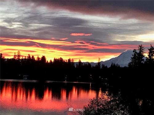 a sunset over a lake with a mountain in the background at Beautiful Lake Lodge with Huge Private Dock in Spanaway
