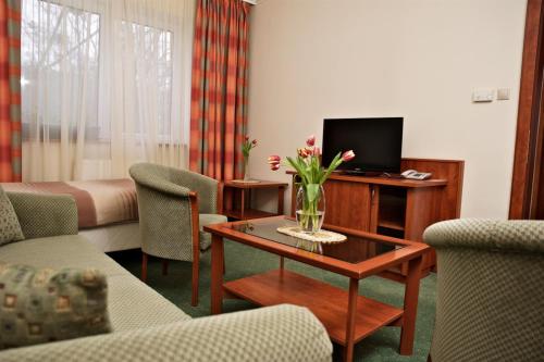 a living room with a table with a vase of flowers on it at Hotel Lukács Superior in Kazincbarcika