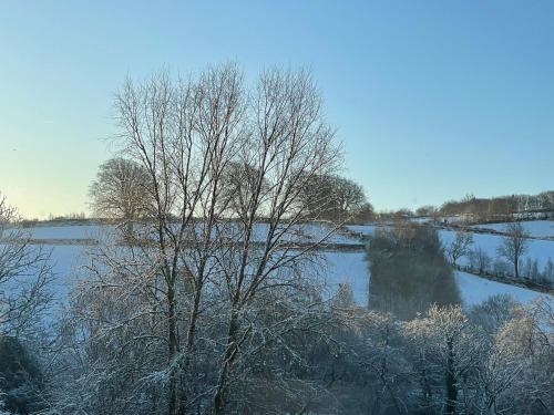 a snow covered field with a river and trees at The Hayloft, Exmoor in Withypool