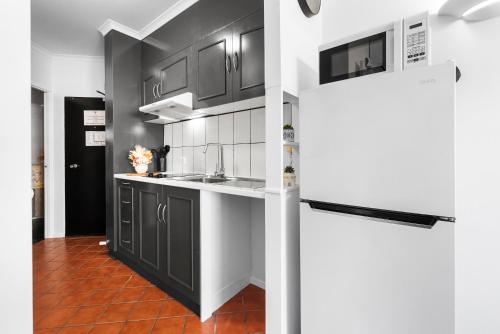 a kitchen with black cabinets and white appliances at Villa Vaucluse Apartments in Cairns