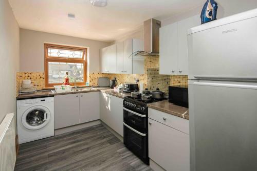 a kitchen with white cabinets and a washer and dryer at Huge 6 Beds House in Zone 2 London-MobileRateOffers-Families-Leisure-Parking-WiFi-PoolTable-Netflix-Sleeps15! in London