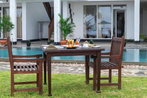 a wooden table and two chairs in front of a pool at Shavara Beach in Ahangama