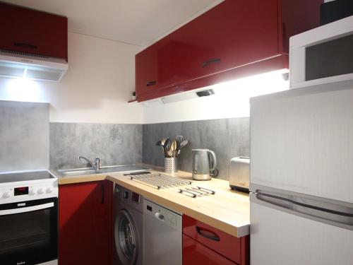 La cuisine est équipée de placards rouges et d'un four avec plaques de cuisson. dans l'établissement Appartement 2** proche pistes avec parking - 5 couchages - Mont-Dore - FR-1-415-114, à Le Mont-Dore