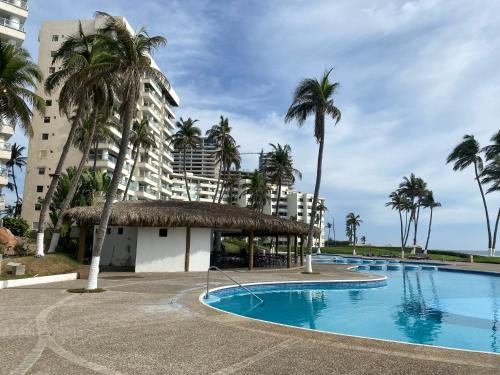 a swimming pool with palm trees and a building at Mayan Playa Departamento Uxmal in Acapulco
