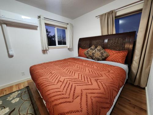 a bedroom with a bed with an orange comforter and two windows at Comfortable Jacksonville house in Medford