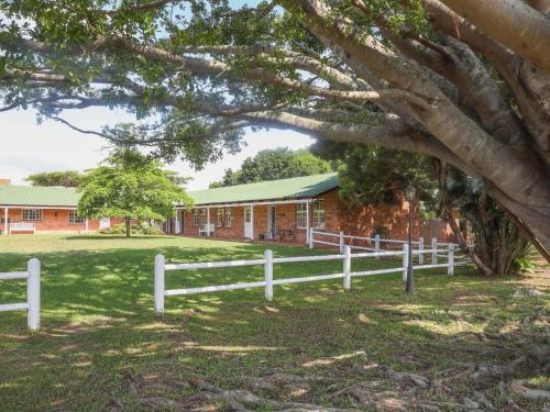 une clôture blanche devant un bâtiment en briques avec un arbre dans l'établissement Fountainhill Estate Accommodation, à Wartburg