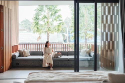 a woman sitting on a couch in front of a window at Villa De Time - The Luxury Private Pool Villa in Pattaya South