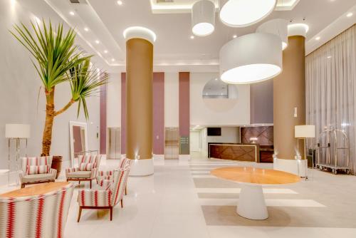 a lobby with chairs and a table and a palm tree at Linx Confins in Confins