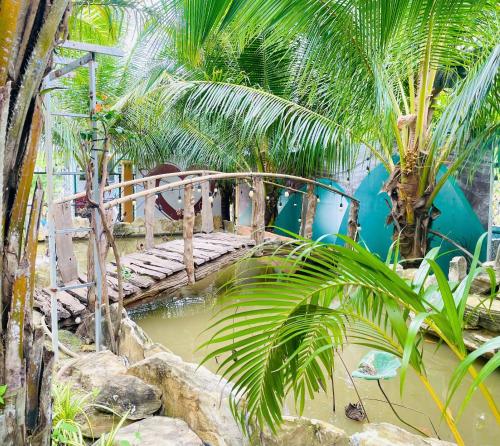 a bridge over a pond in a garden with palm trees at The Lana Ho Tram Homestay in Xuyên Mộc