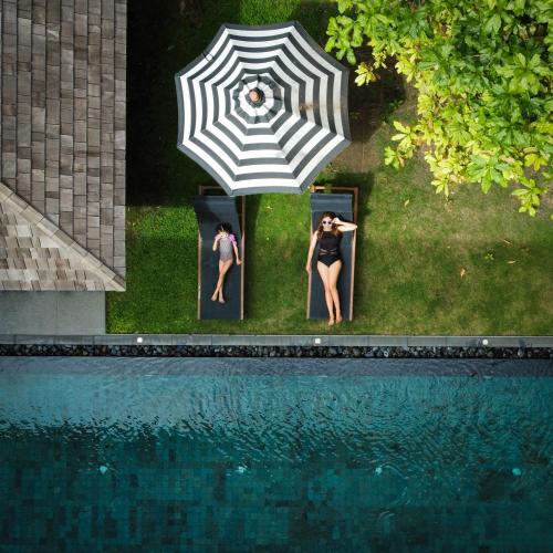 two people standing under an umbrella next to a swimming pool at Villa De Time - The Luxury Private Pool Villa in Pattaya South