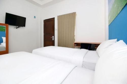 two white beds in a room with a television at RedDoorz Plus Syariah at Polamas Andalas in Padang