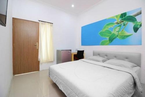 a bedroom with a white bed and a painting on the wall at RedDoorz Plus Syariah at Polamas Andalas in Padang