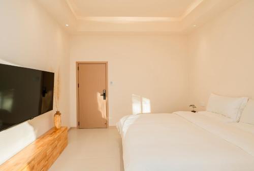 a white bedroom with a large bed and a flat screen tv at Yunyuan Private Hot Spring Bed and Breakfast in Sanying
