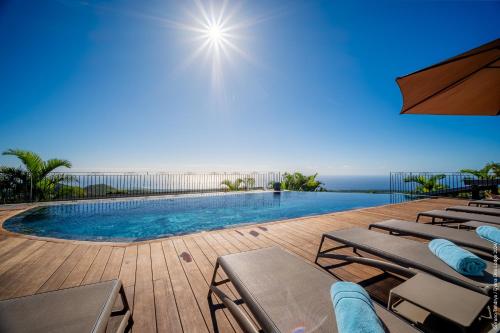 a swimming pool with chaise lounge chairs and the ocean at Hôtel Diana Dea Lodge & SPA in Sainte-Anne-les Hauts