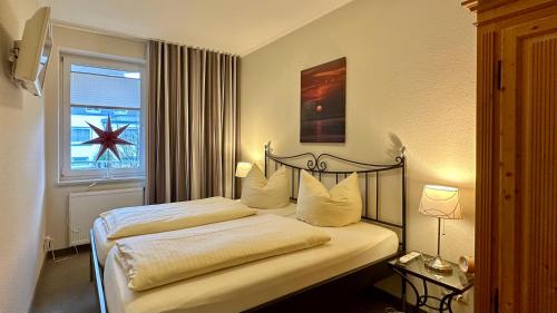 a bedroom with a bed with white sheets and a window at Ferienwohnungen Auf der Düne in Cuxhaven