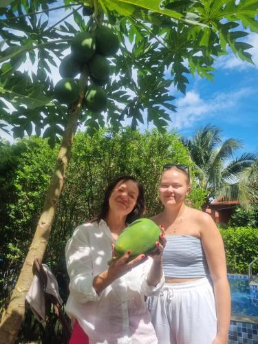 two women standing under a fruit tree holding a melon at AnAn Boutique Bungalows with Private Kitchen in Phu Quoc