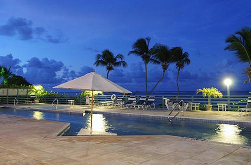 a swimming pool with chairs and an umbrella and the ocean at Club St. Croix Beach and Tennis Resort in Christiansted