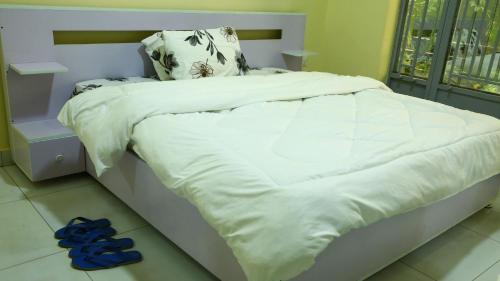 1 cama con sábanas blancas y zapatillas azules en el suelo en KIGALi LODGE APART, en Kigali