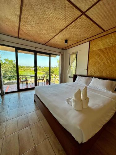 a bedroom with a large white bed with a view at บ้านกลางเกาะ รีสอร์ท in Uthai Thani