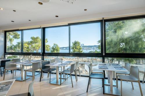 a dining room with tables and chairs and large windows at Els Pins Resort & Spa - Emar Hotels in San Antonio Bay
